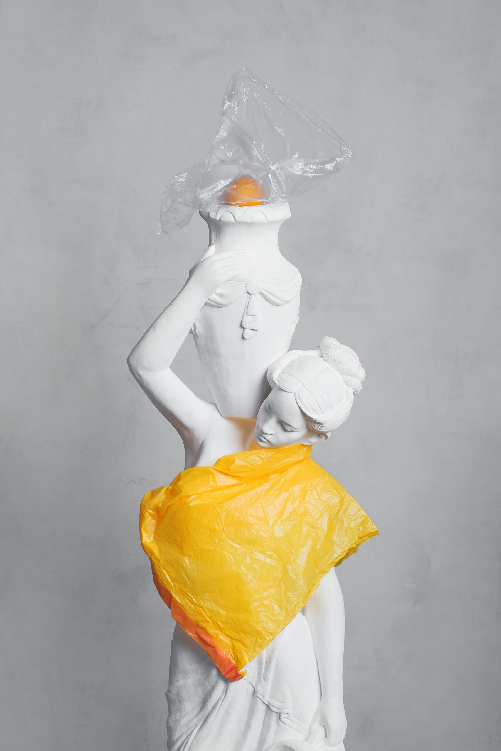 A white statue wrapped in vibrant plastic bags highlighting modern pollution.
